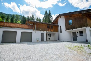 A building with two garages, a wooden balcony, and a gravel courtyard. - Exclusive Alpine Chalet in Niederau (Hopfgarten im Brixental)