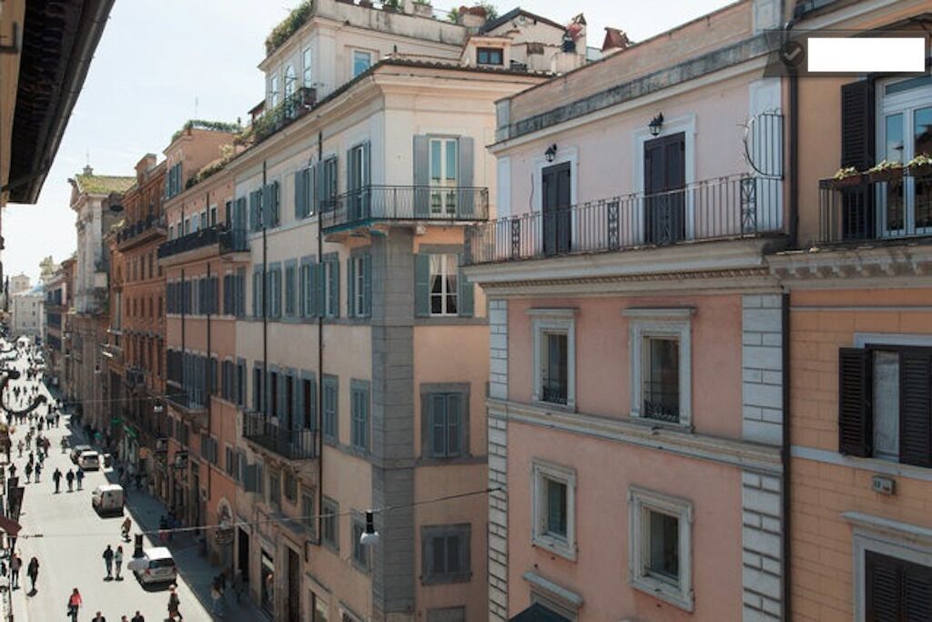 A street lined with multi-story buildings, featuring balconies and windows with shutters.