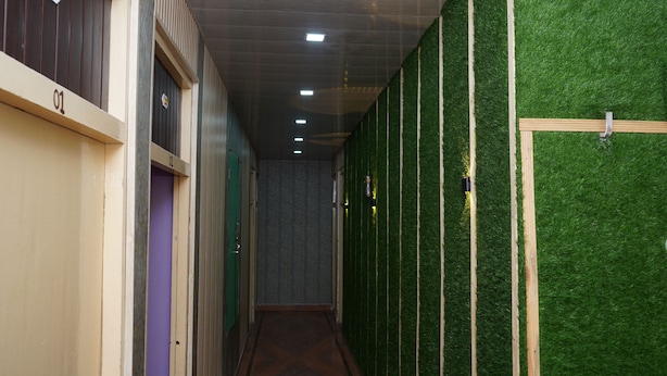 A hallway with artificial green grass walls, numbered doors, and a wooden door on the right.