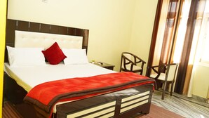 A hotel room with a bed, a nightstand, a chair, and a window with curtains.