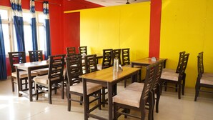 A restaurant with wooden tables and chairs, a bright yellow and red wall, and blue curtains.