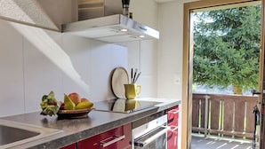 A modern kitchen with a stainless steel range hood, a bowl of fruit on the counter, and a sliding glass door leading to a balcony with a wooden deck. - Stunning  villa for 3 people with TV, patio, pets allowed and panoramic view (Habkern)