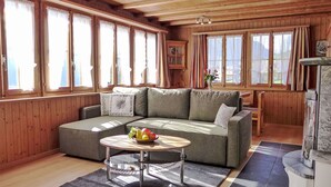 A cozy living room with a sectional sofa, a round coffee table with fruit, and large windows with curtains. - Stunning  villa for 3 people with TV, patio, pets allowed and panoramic view (Habkern)