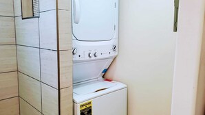 A compact, white laundry room with a built-in washer and dryer, a vent above the dryer, and a yellow energy efficiency label on the dryer. - The Studio on Polk - Cozy Downtown Studio! (Brownsville)