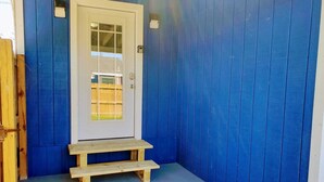 A blue-painted exterior with a white door, a small wooden bench, and a welcome mat. - The Studio on Polk - Cozy Downtown Studio! (Brownsville)