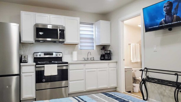 A compact kitchen with white cabinets, a microwave, a stove, and a coffee maker. - The Studio on Polk - Cozy Downtown Studio! (Brownsville)