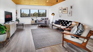 Un salon moderne avec un plafond en bois, une grande fenêtre, un téléviseur, un canapé et une table basse.