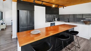 Une cuisine moderne avec un îlot central en bois, des tabourets de bar noirs et un réfrigérateur en acier inoxydable.