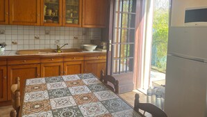 A kitchen with wooden cabinets, a tiled backsplash, a sink, and a dining table with patterned tablecloth. - Town/country house 6 km from Tours, fitted kitchen, garden, pets welcome. (Fondettes)