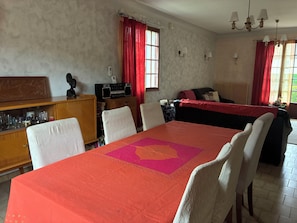 Un comedor con una mesa dispuesta para cuatro personas, sillas, una radio en un mueble y un sofá al fondo.