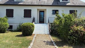 A two-story house with a front door, two windows with shutters, a small porch, and a gravel pathway leading to the door. - Town/country house 6 km from Tours, fitted kitchen, garden, pets welcome. (Fondettes)