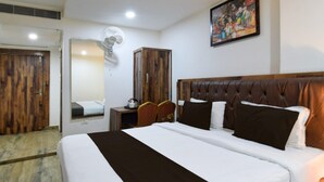 A hotel room with a large bed, a wooden wardrobe, a mirror, a fan, and a painting on the wall. - Elegant Stays at Vanasthalipuram Hyderabad (Hyderabad)