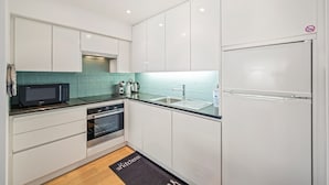 A modern kitchen with white cabinets, a black countertop, a microwave, an oven, and a refrigerator.