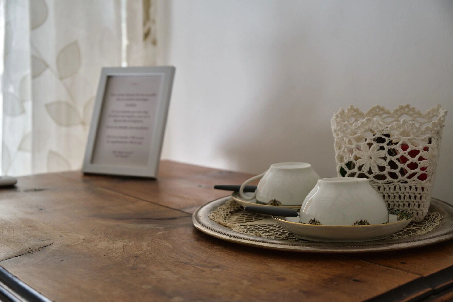 A table with a tray holding two cups and a teapot, a framed menu, and a crocheted basket.
