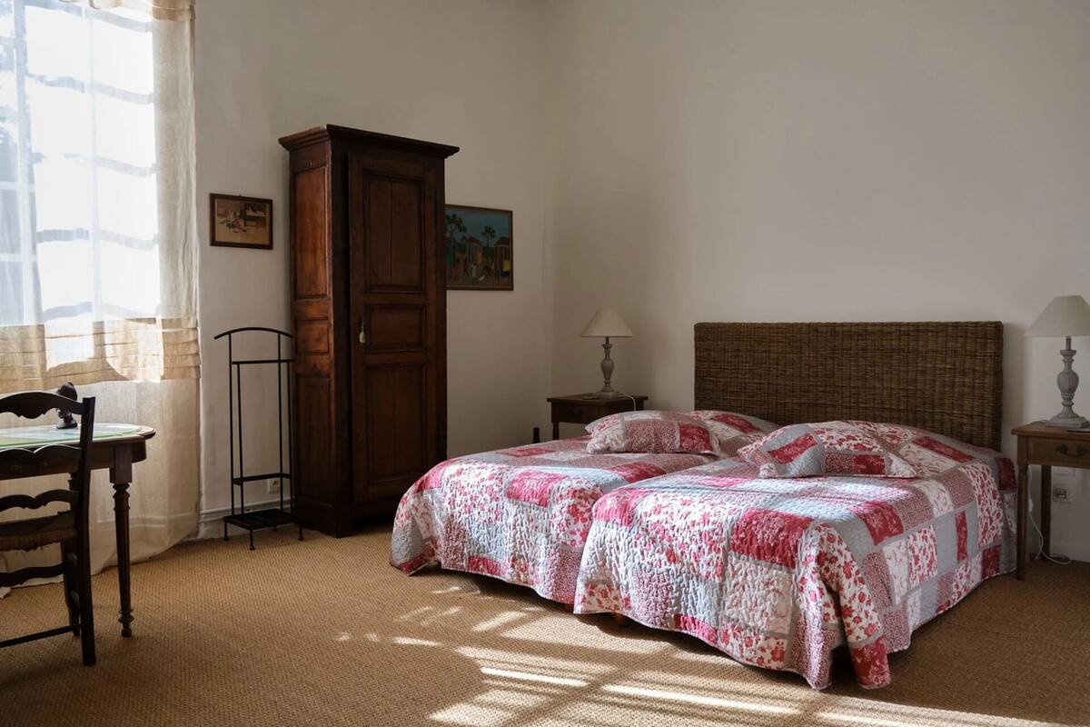 Een slaapkamer met een bed, twee nachtkastjes, een houten garderobe en een bureau met een stoel.