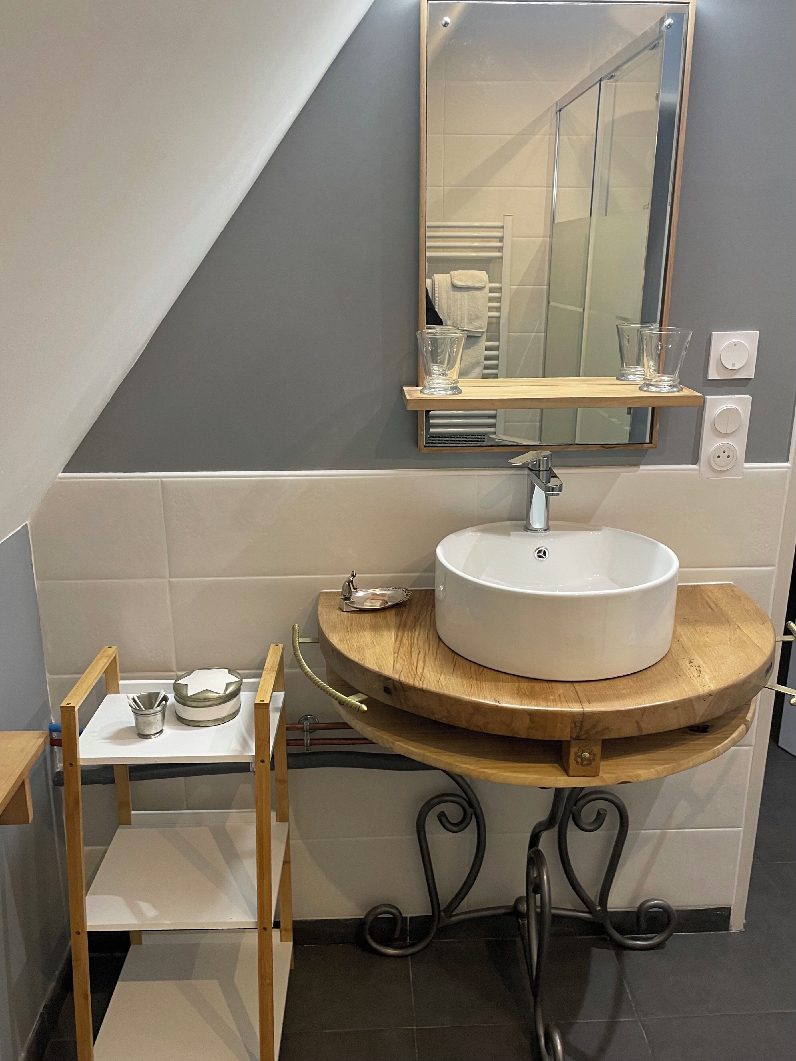 Un baño con un lavamanos blanco, un mueble de tocador de madera, un espejo y un taburete pequeño.