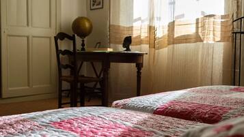 Un dormitorio con dos camas, un escritorio con un globo terráqueo, una silla y una ventana con cortinas.