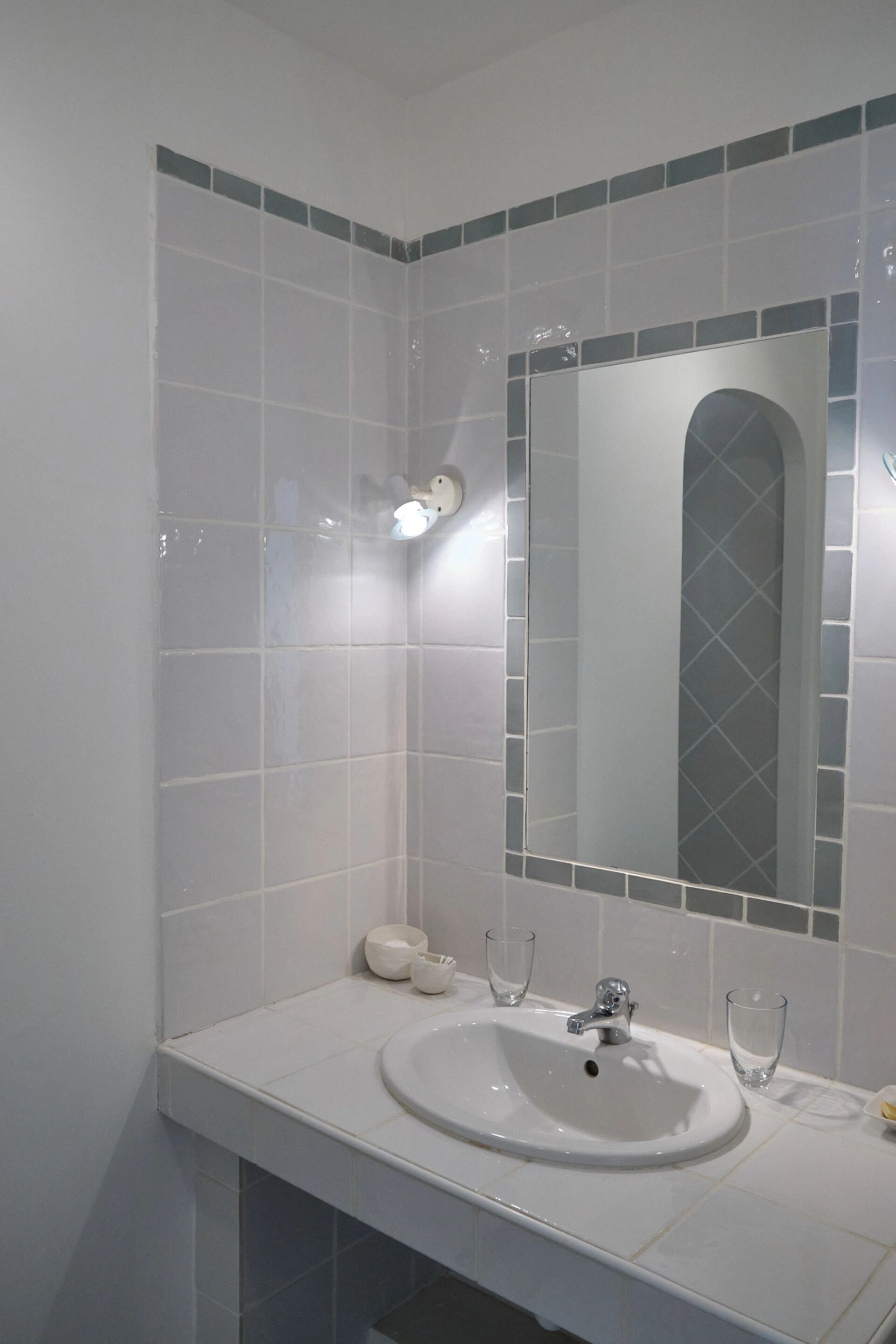 A bathroom with a white sink, a mirror, and a tiled wall.