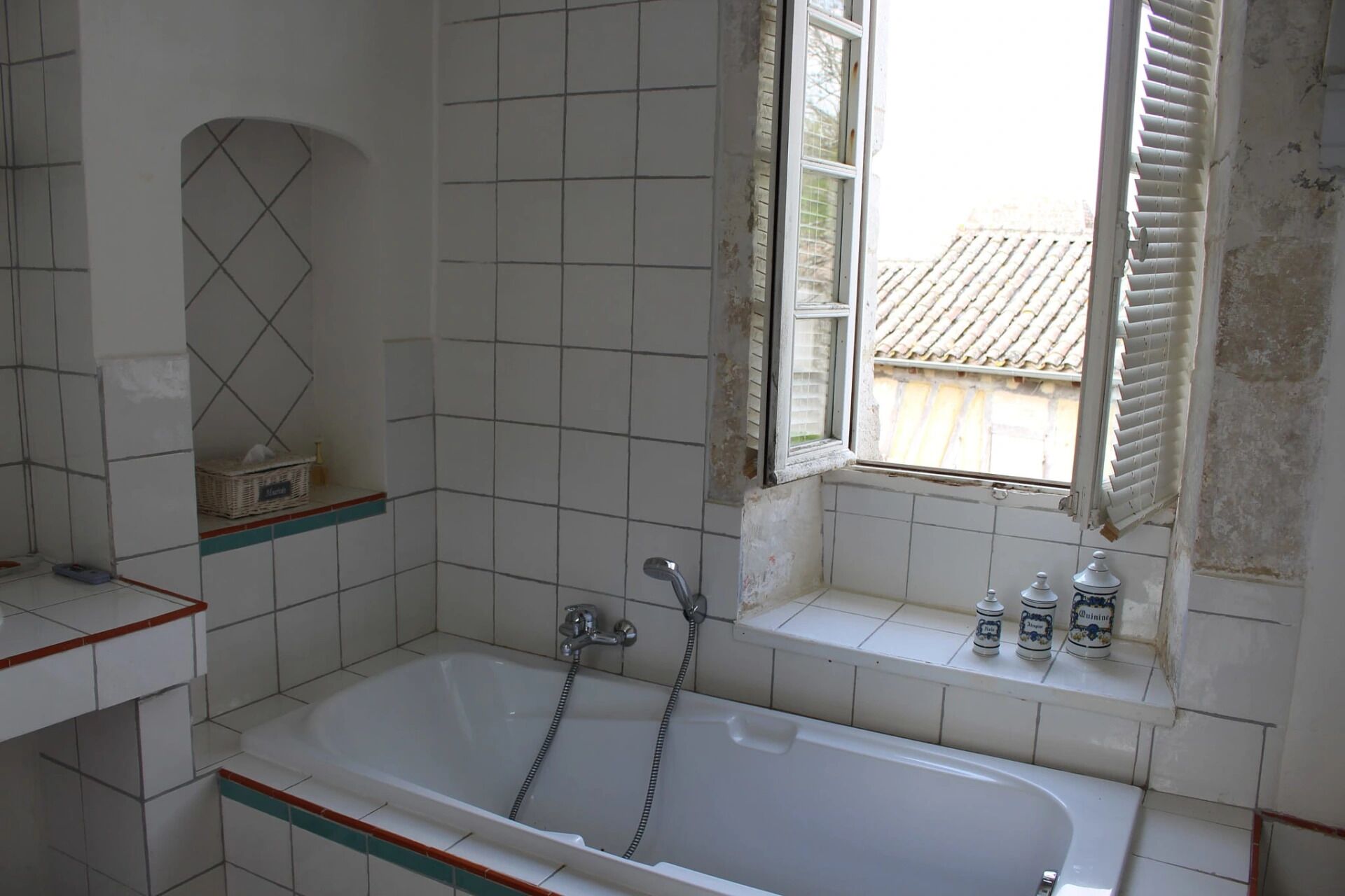Une salle de bain avec une baignoire, une fenêtre avec des volets et des murs carrelés.