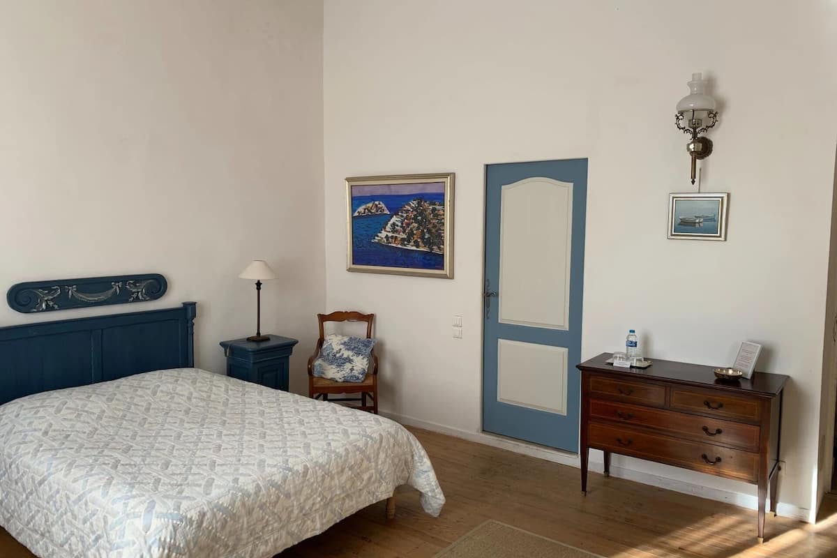 Een slaapkamer met een bed, een stoel, een dressoir, een deur en wanddecoratie.