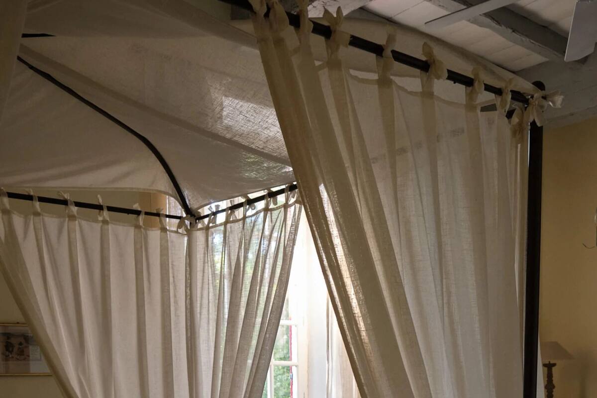 Een hemelbed met bloemenbeddengoed, een raam met uitzicht en een radiator.