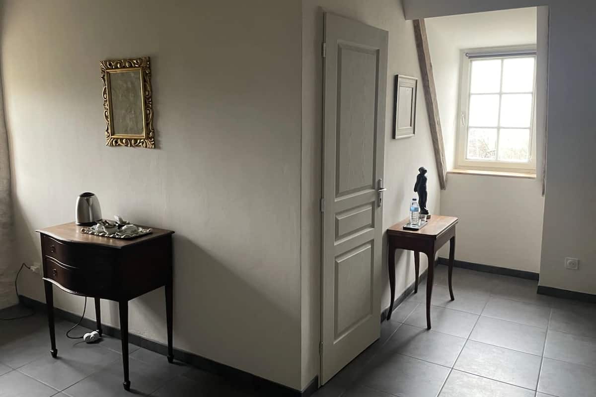 Een kamer met een bureau, een stoel, een klein tafeltje met een beeldje, een spiegel en een raam met natuurlijk licht.