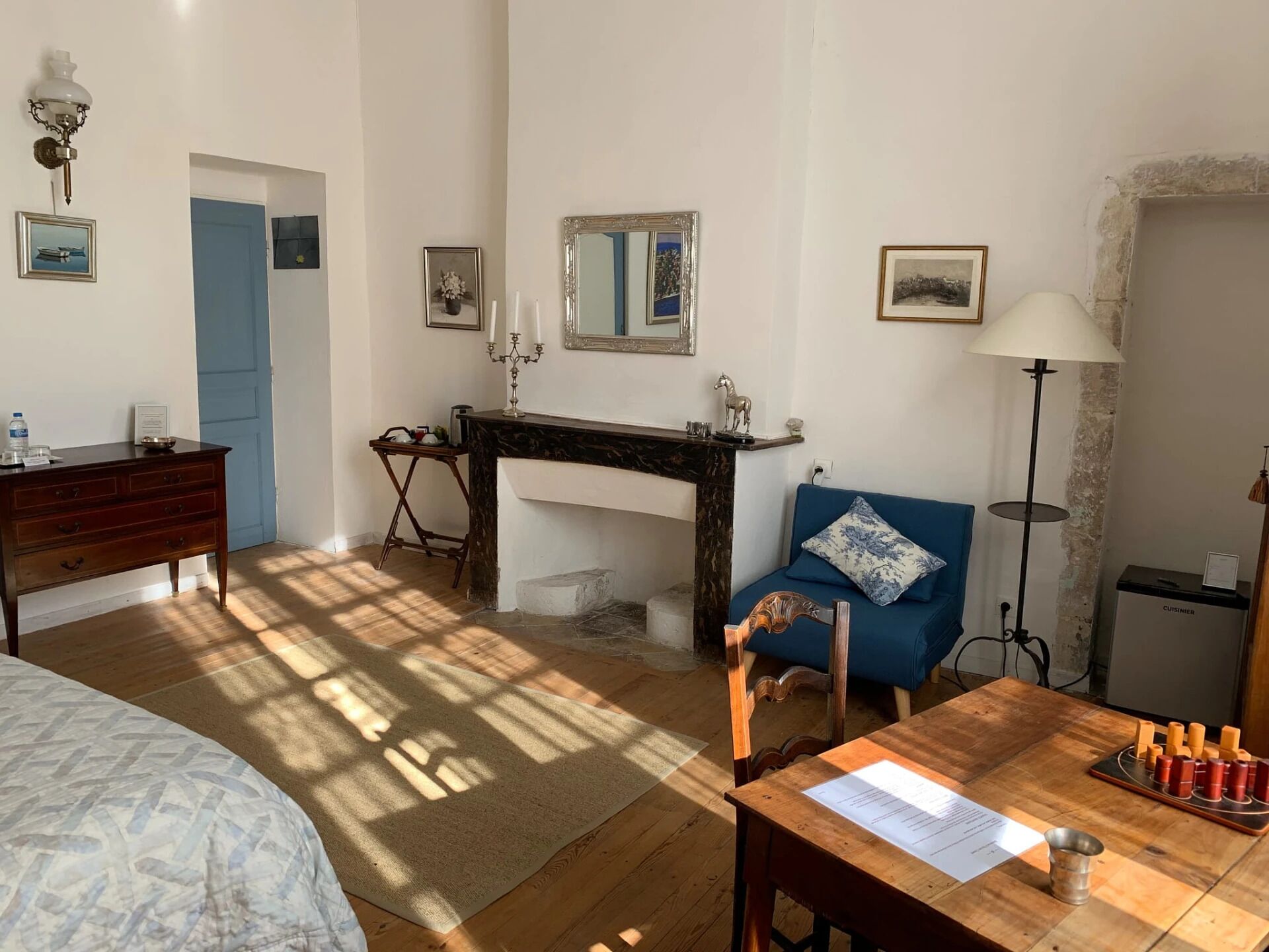 A room with a bed, a desk, a chair, a table with a menu, and a lamp.