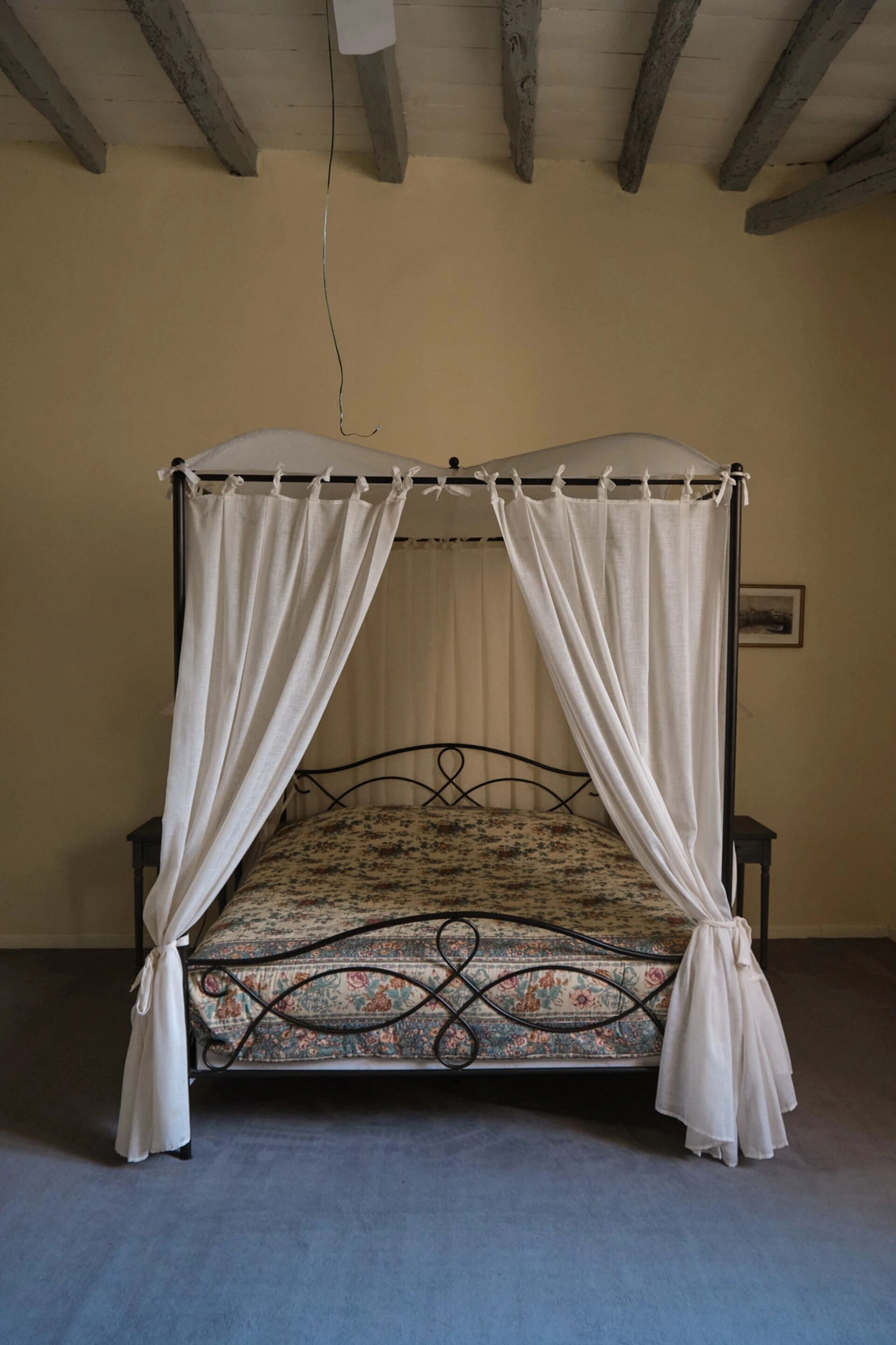 Ein Bett mit Baldachin, ein blumenmusteriges Matratze und weiße Vorhänge.