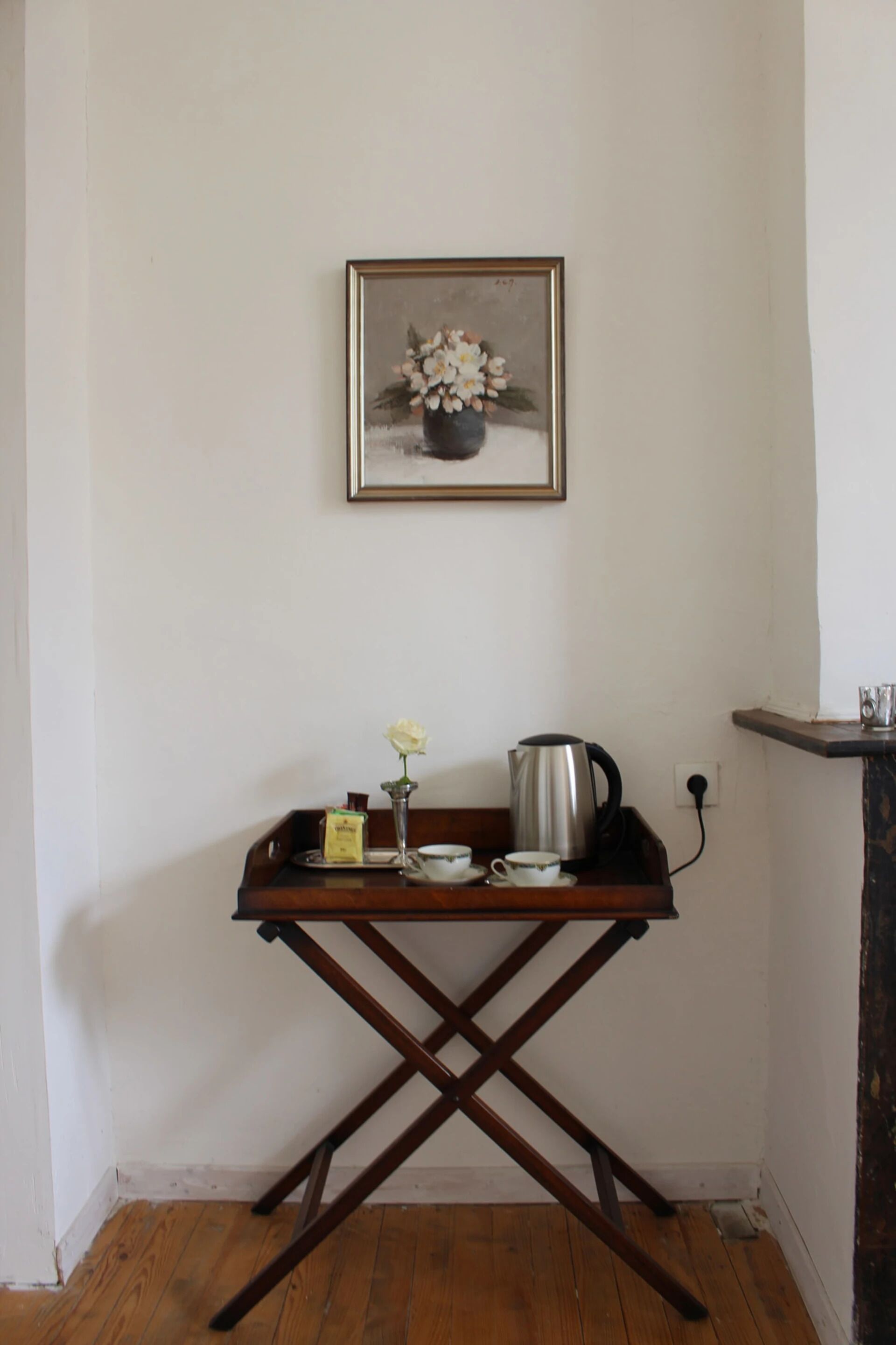 Una pequeña mesa de madera con una bandeja que contiene una tetera, tazas y un florero con flores.