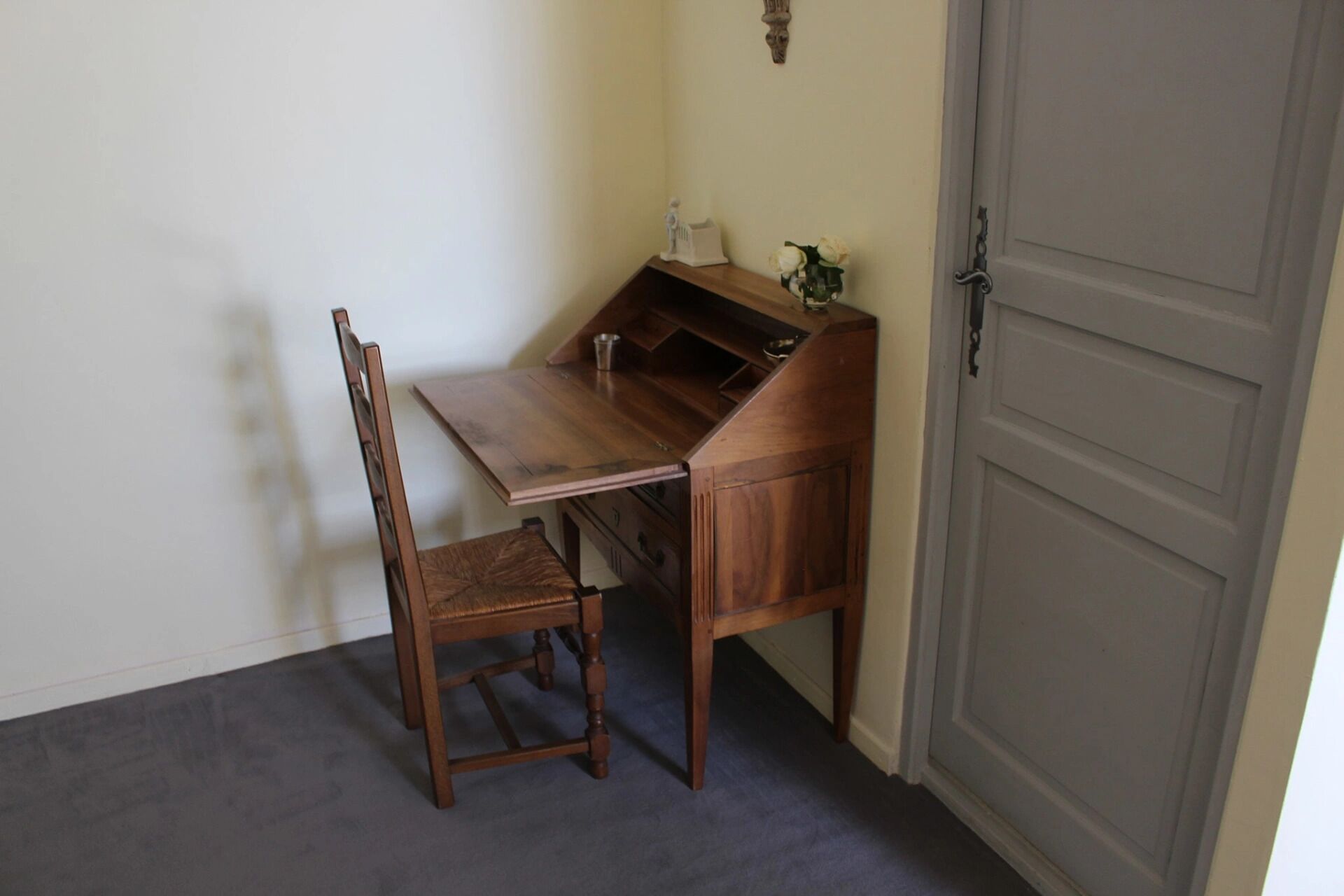 Ein Holztisch mit einem Stuhl in einem Raum mit geschlossener Tür und einem kleinen Regal mit Dekoration.