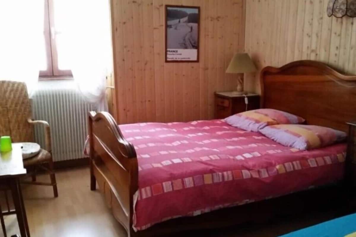 Ein Schlafzimmer mit einem hölzernen Bett, einem Sessel, einem Tisch mit einer Flasche und einem Poster an der Wand.