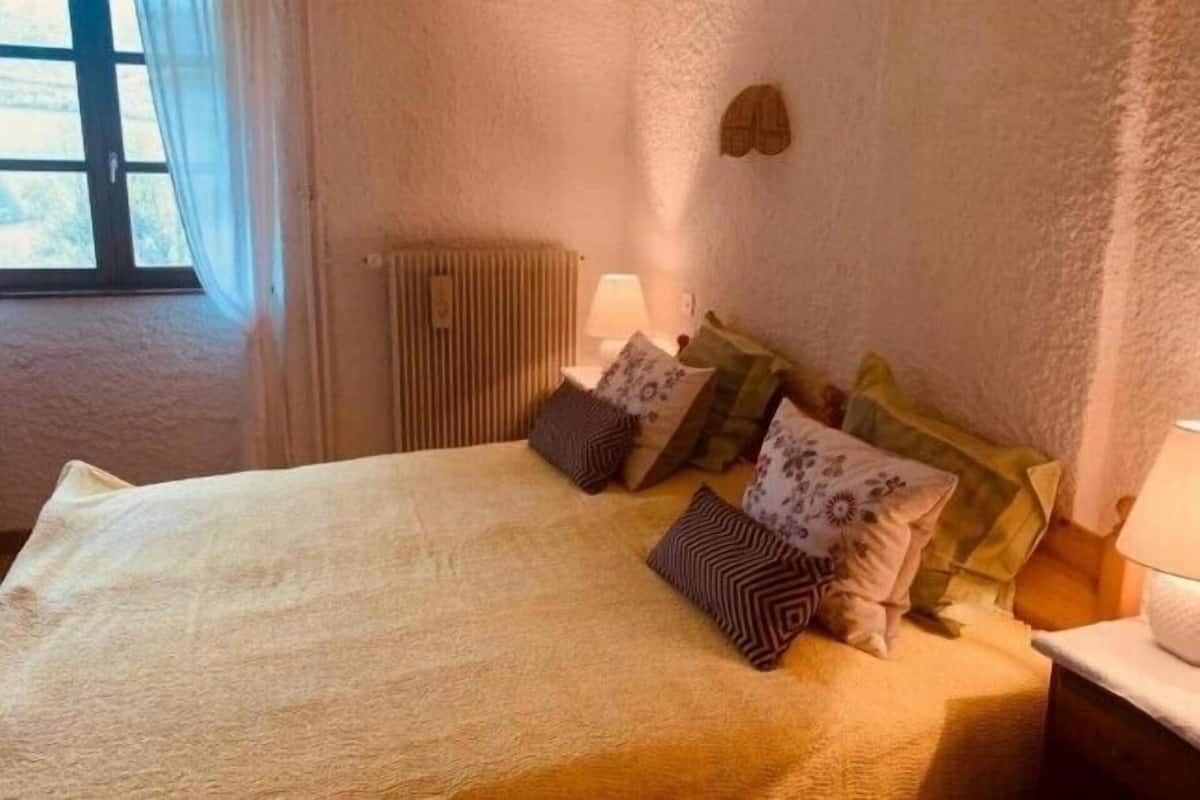 Ein Schlafzimmer mit Bett, Kissen, Nachttisch, Lampe und Heizkörper.