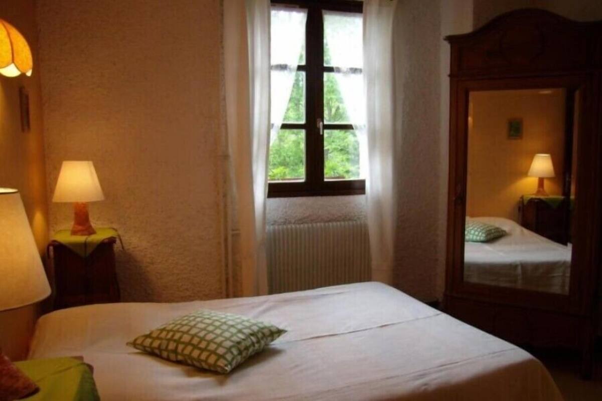 Ein Schlafzimmer mit Bett, Fenster, Heizkörper, Spiegel und zwei Nachttischlampen.