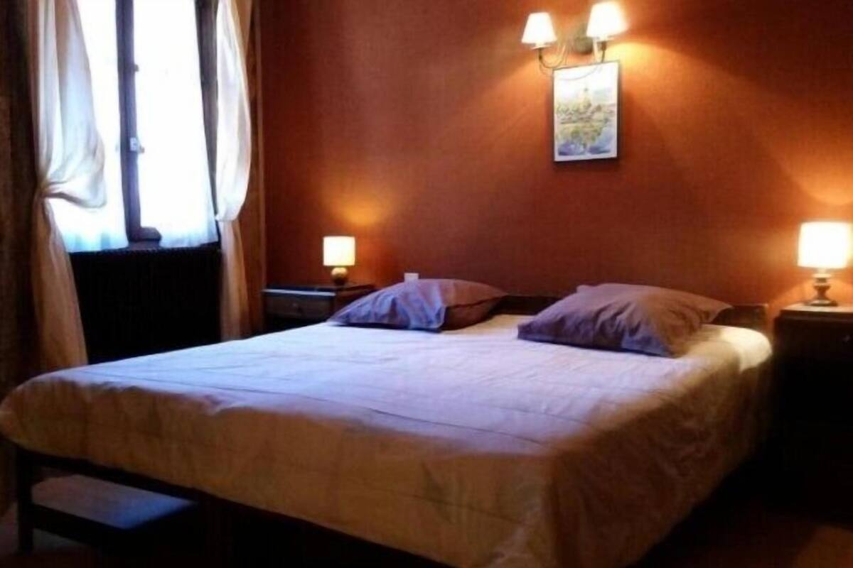Ein Hotelzimmer mit einem Bett, zwei Nachttischlampen, einem fensterbelaubten Fenster und einem Wandbild.