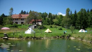 A lakeside setting with several tents and a house in the background. - Le Castel Blanc (Chatelblanc)