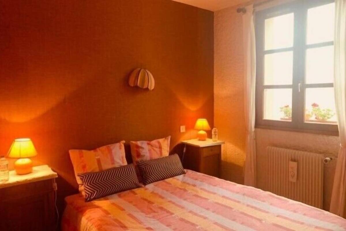 Ein Schlafzimmer mit einem Bett, zwei Nachttischlampen, einem Fenster mit Vorhängen und einer Heizung.