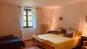 A bedroom with a double bed, a single bed, a nightstand, a lamp, and a window with curtains. - Le Castel Blanc (Chatelblanc)