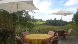 A wooden deck with a round table and chairs, two large umbrellas, and a view of a green landscape. - Le Castel Blanc (Chatelblanc)