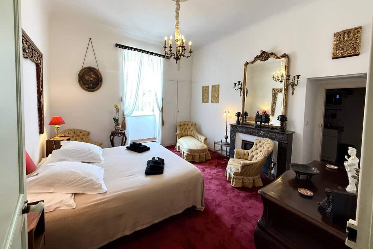 Una habitación de hotel con una cama grande, una chimenea, un candelabro y un espejo.