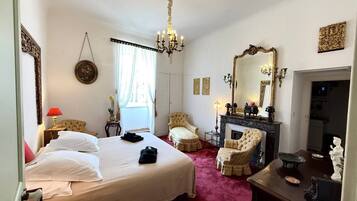 A hotel room with a large bed, a fireplace, a chandelier, and a mirror.