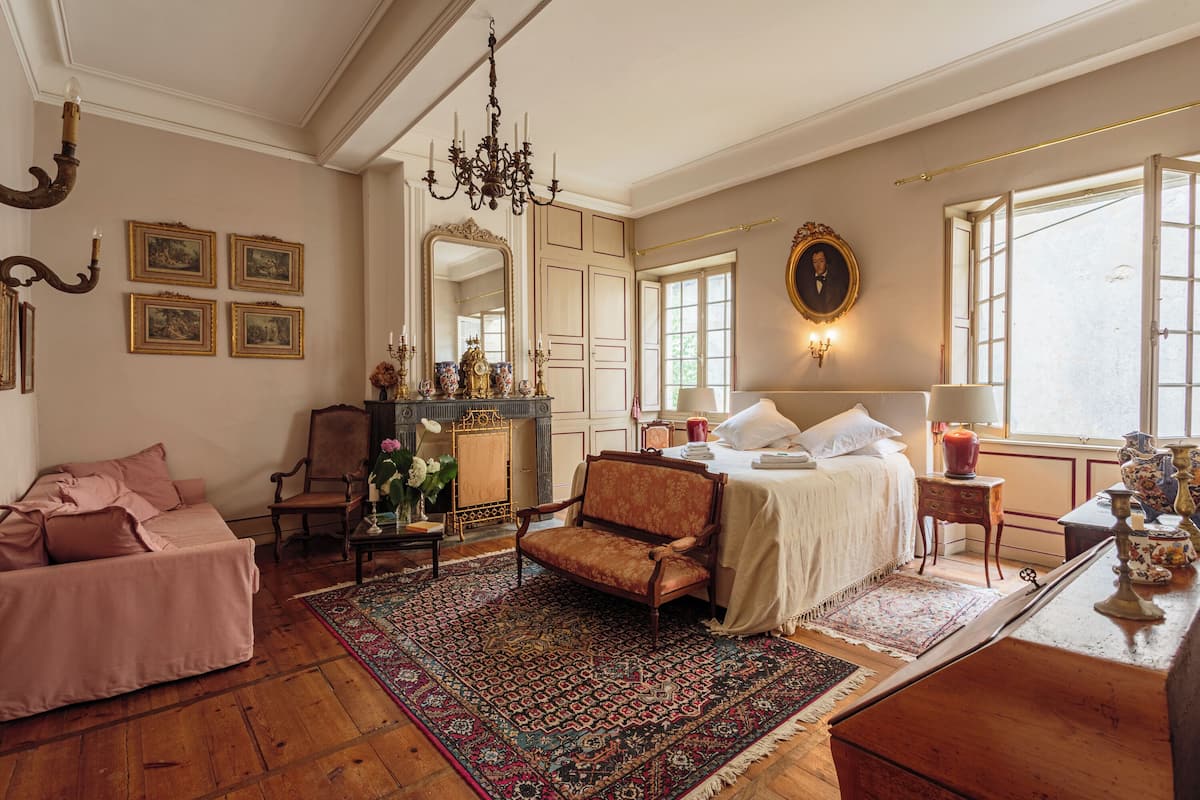 Una habitación con cama, sofá, sillón, chimenea y un espejo grande.