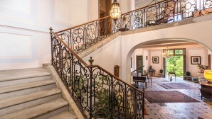 A grand staircase with ornate metal railings, leading to a spacious foyer with a chandelier, rugs, and a piano. - Le Château D'Estrac (Hastingues)