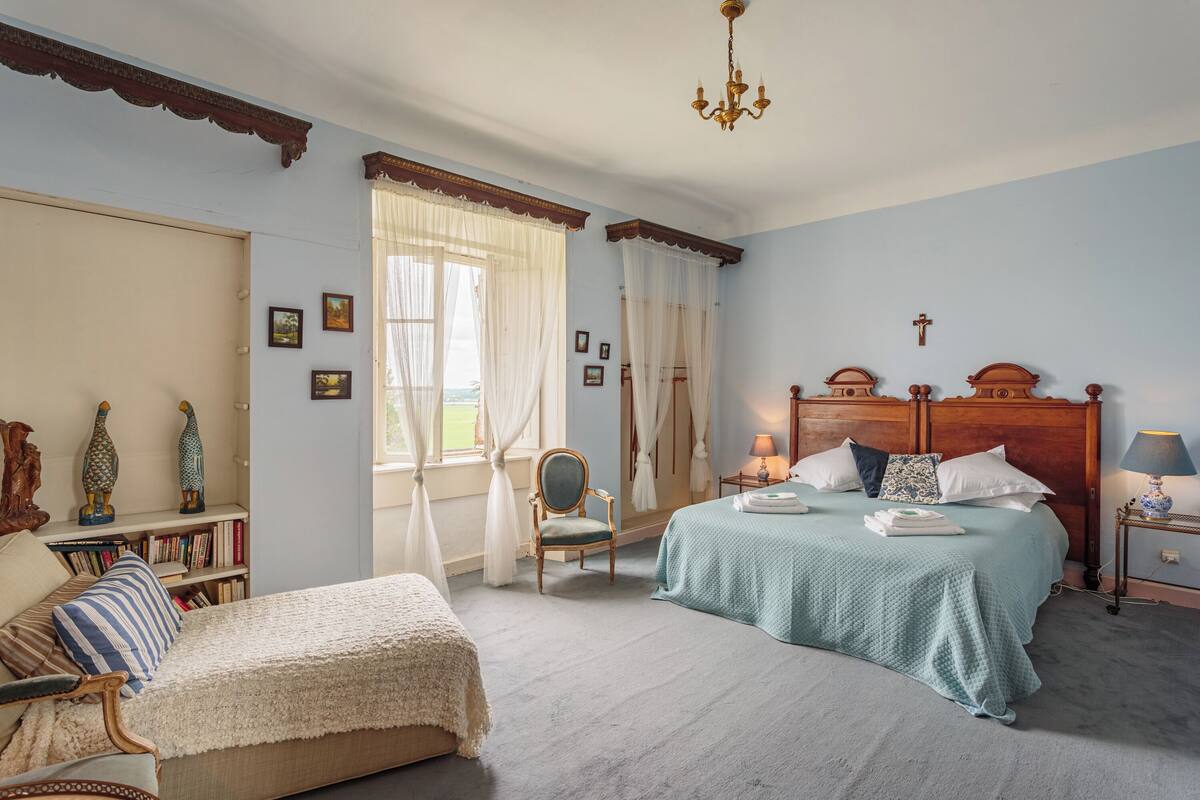 Un dormitorio con cama, una silla, una estantería y una ventana con cortinas.