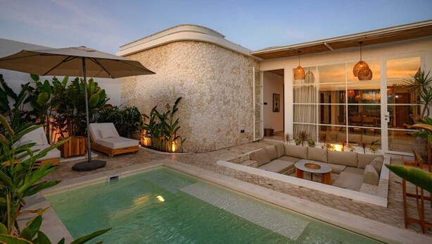 A pool area with a stone wall, outdoor seating, and a large umbrella. - Modern 3 bedrooms pool villa near the beach, shops, and restaurants (Bali)