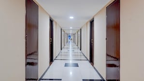 A long, narrow hotel corridor with doors on both sides, a tiled floor, and a ceiling with recessed lighting. - Super Townhouse Koyambedu Royal Plaza (Chennai)
