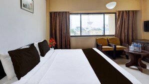 A hotel room with a large bed, a desk with two chairs, a window with curtains, and a view of buildings outside. - Super Townhouse Koyambedu Royal Plaza (Chennai)
