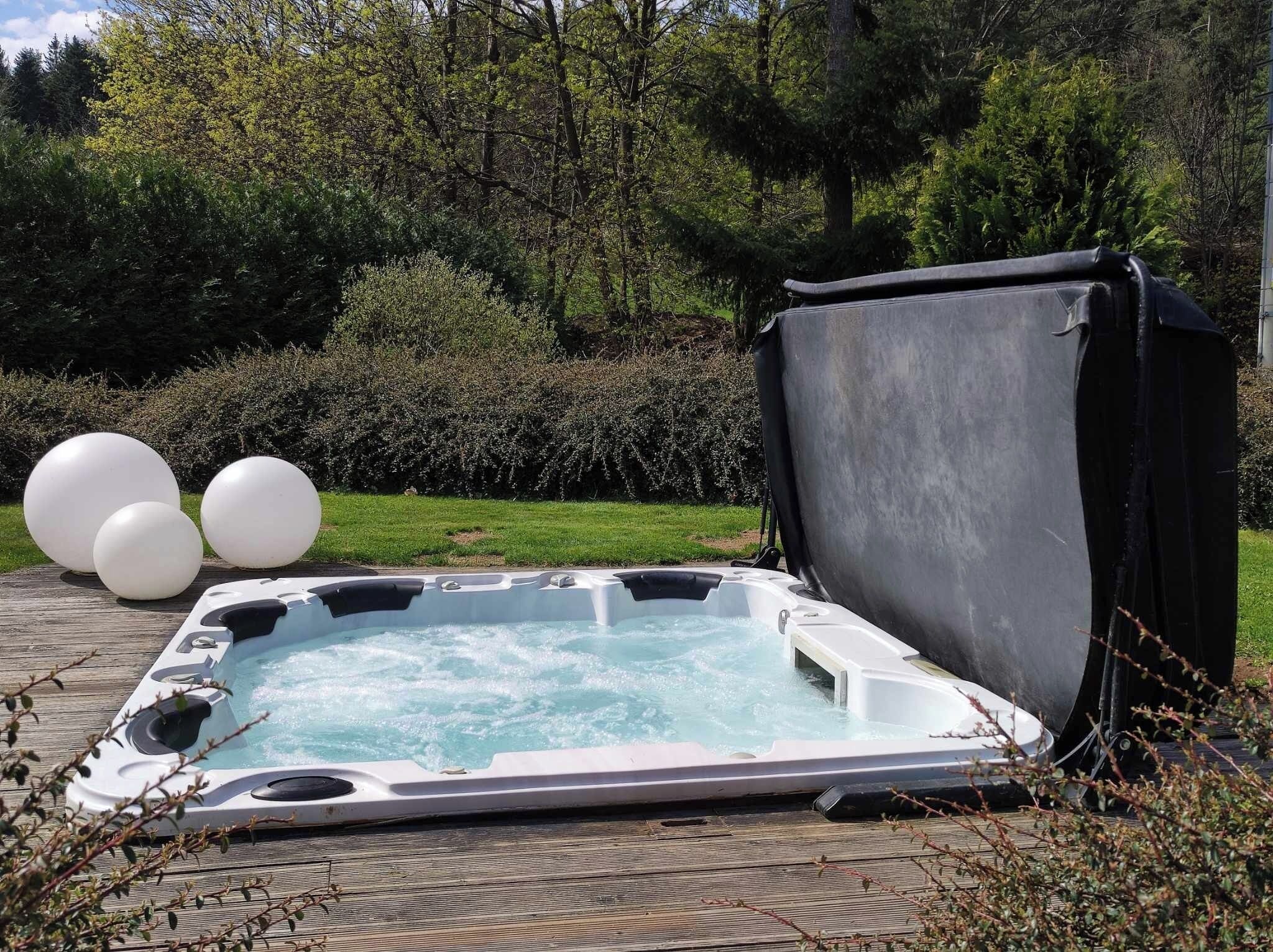 A hot tub outdoors with a cover, surrounded by greenery and three white balloons.