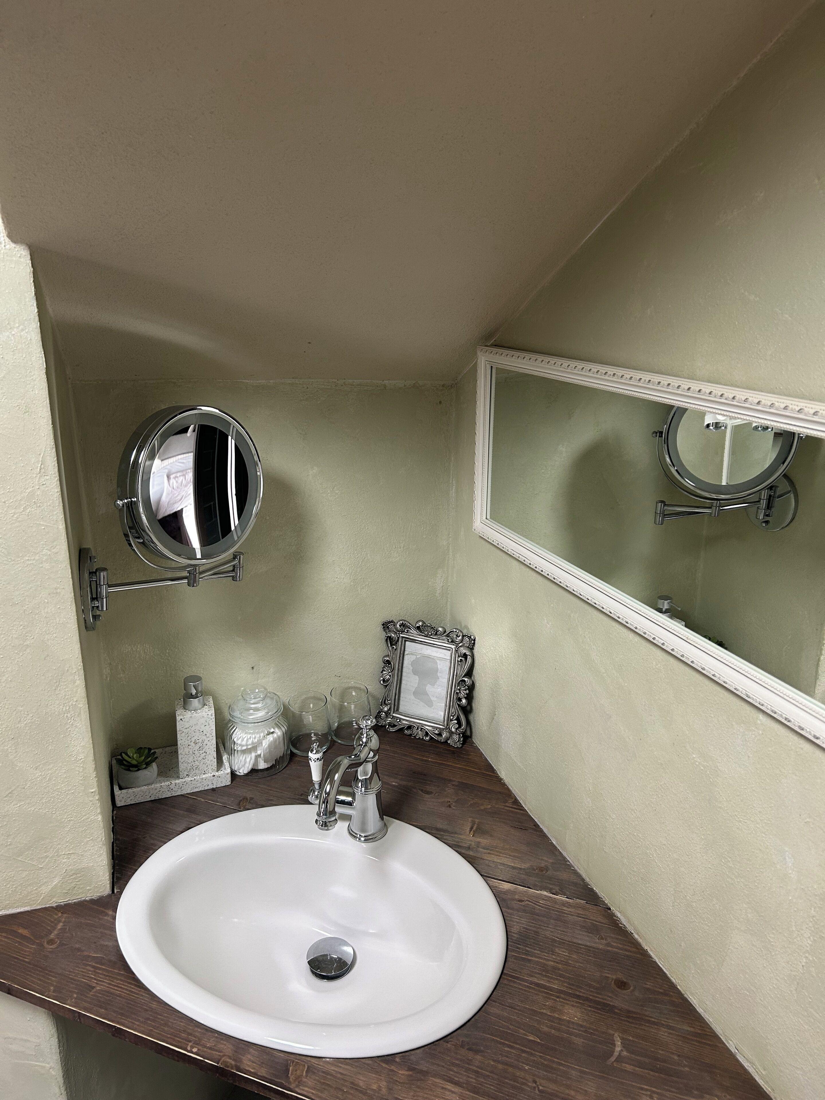 A bathroom with a white sink, two mirrors, a framed picture, and a small shelf with toiletries.