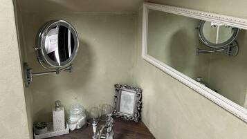 A bathroom with a white sink, two mirrors, a framed picture, and a small shelf with toiletries.
