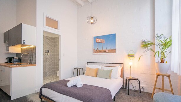 Ein Schlafzimmer mit Bett, Nachttischen, einem Schreibtisch mit Stuhl, einer Dusche und einer Wandleuchte.